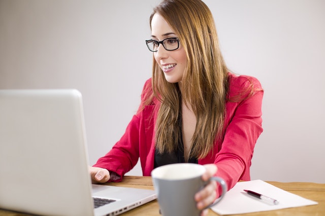 žena v rudém saku s počítačem a kávou